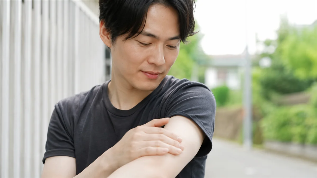 屋外の自然光の中で自分の前腕の肌を確認する男性